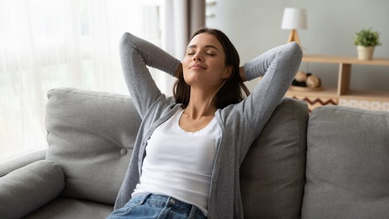 Woman Relaxed On Couch With Arms Clasped Behind Head